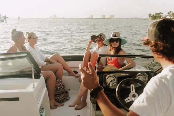 Four people relax on a boat cruising on open water under a clear sky.
