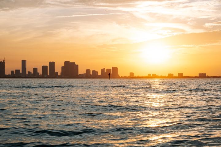 City skyline at sunset with ocean in the foreground.