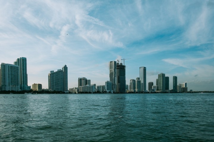 Skyline of a city with tall buildings and a waterfront under a blue sky.