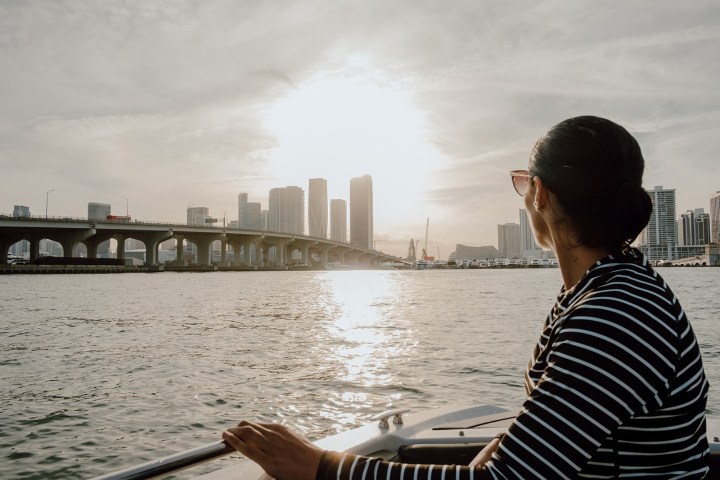 Person on a boat, looking at a city skyline and bridge during sunset.