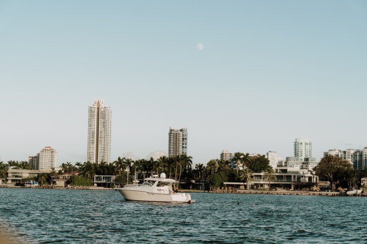 Boat on water with city skyline and palm trees in the background under a clear sky.