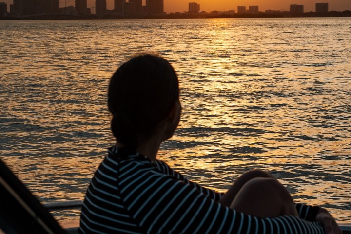 Person on boat watching sunset over city skyline and water.